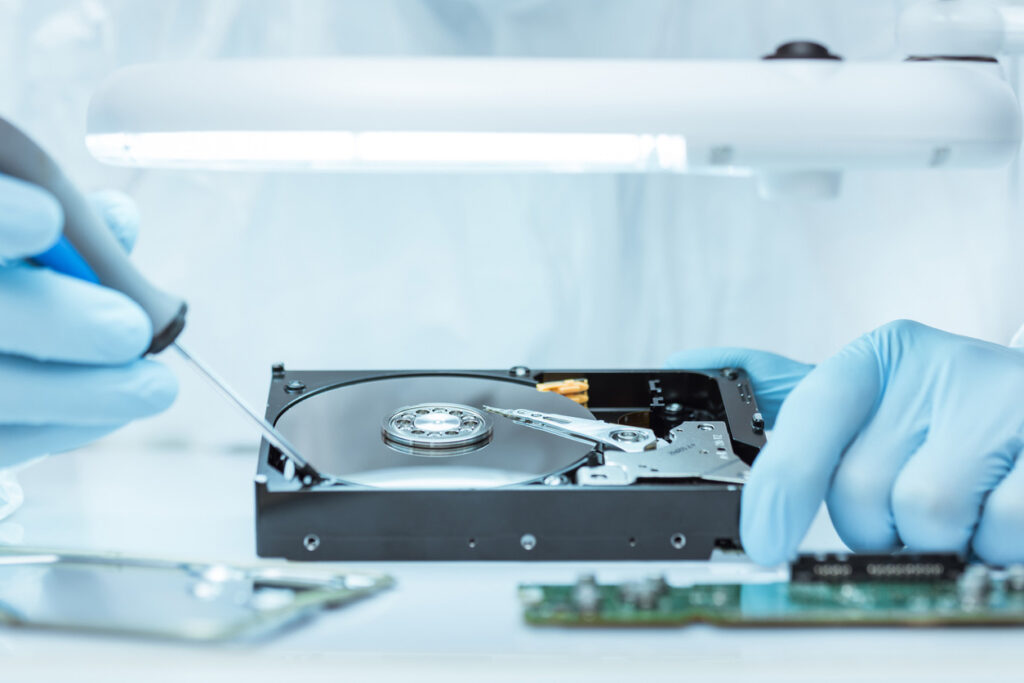 Engineer handling an exposed hard drive, highlighting data security risks of improper or non-compliant IT asset disposal