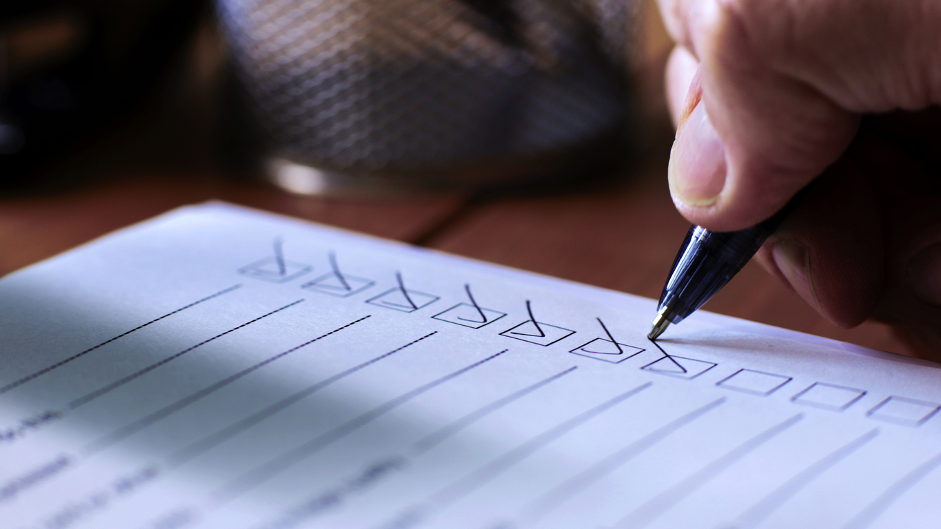 Hand checking off items on a checklist, symbolizing the evaluation criteria for selecting an ITAD vendor in the context of secure and compliant IT asset disposal.