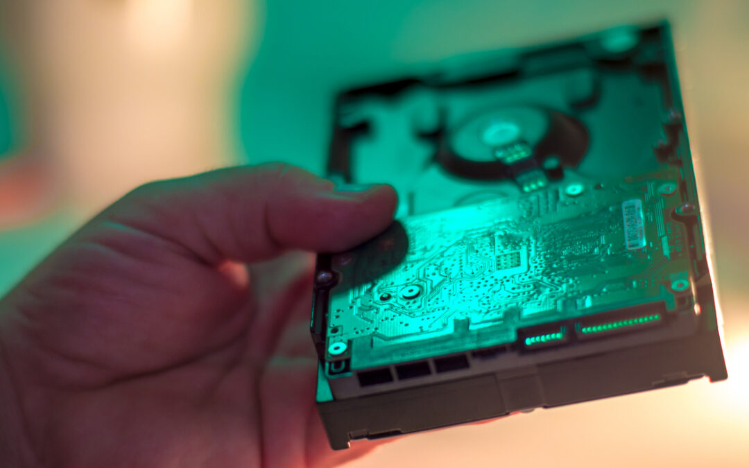 Hand holding a hard drive with intricate circuitry, emphasizing secure IT asset disposal and data destruction services by Astralis Technology.