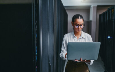 Woman using a laptop in a data centre, illustrating IT asset management and secure data handling in the context of IT asset disposition strategies.