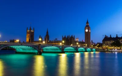London's Houses of Parliament and Big Ben illuminated at dusk, reflecting in the Thames River.