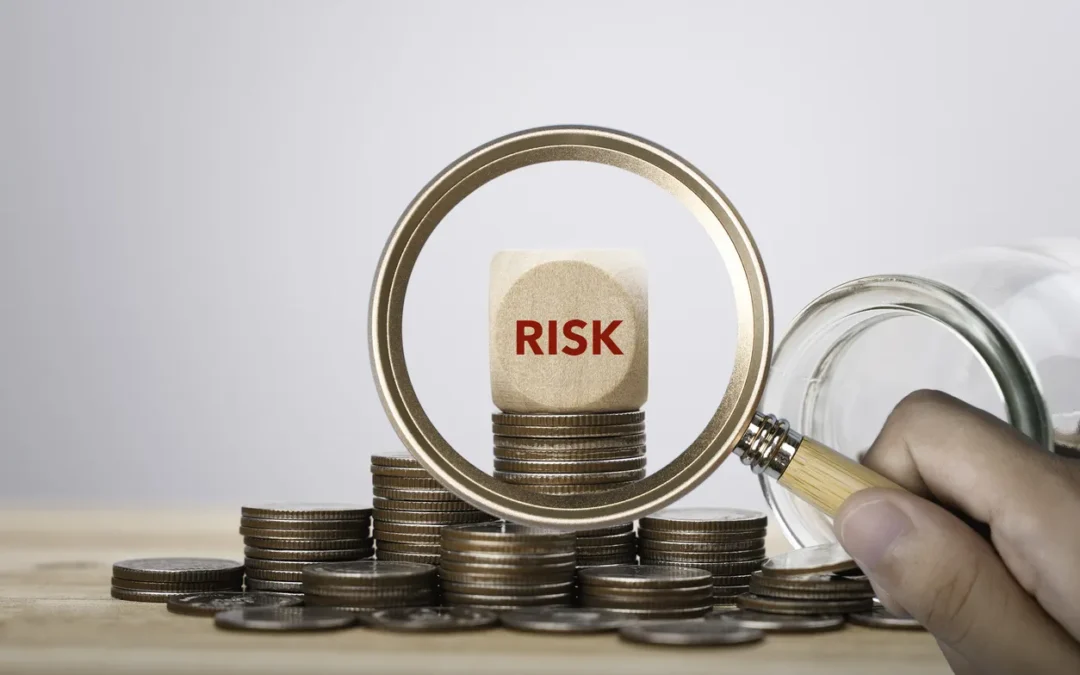 A magnifying glass highlighting the word “risk” on a wooden block placed on stacked coins, representing financial exposure, compliance risk and the importance of scrutiny in IT asset decisions.