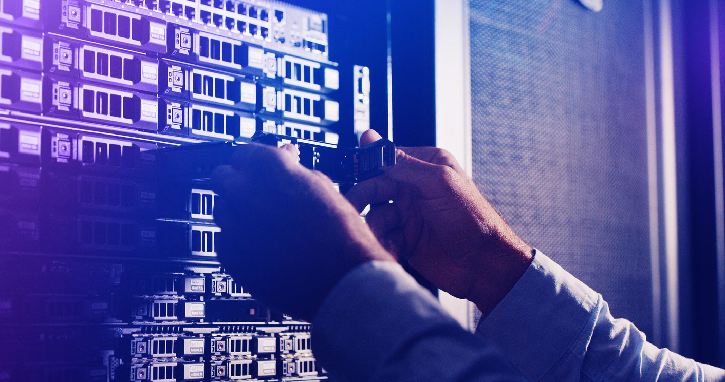 Man inspecting a hard drive within a modern data centre environment, surrounded by server racks and network infrastructure, representing secure IT asset handling and data management.<br />
 